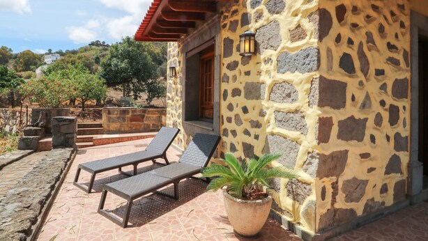 A stone building with a red roof, a potted plant, and two lounge chairs outside. - Countryside Views House Teror 1 (Teror)