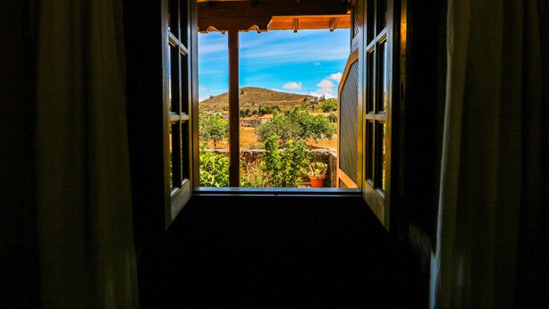 En åben dør, der fører til en balkon med udsigt over et bakket landskab.