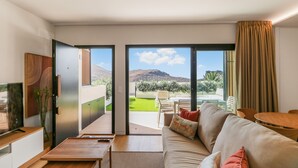 Una sala de estar moderna con un sofá, una mesa de centro y vistas a un jardín verde y montañas.