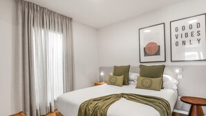 Un dormitorio ordenado con cama, almohadas, mesita de noche, lámpara de pared e imagen enmarcada.