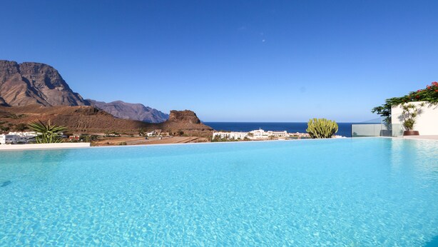 Piscina azul cristalina con montañas al fondo y vista al mar.