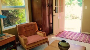 A room with a wooden armchair, a small table with a vase, a wooden cabinet, and a door leading outside. - Redwood coast farm stay (Bayside)