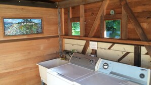 A laundry area with a front-loading washer and dryer, wooden walls, and a window with a view of greenery. - Redwood coast farm stay (Bayside)
