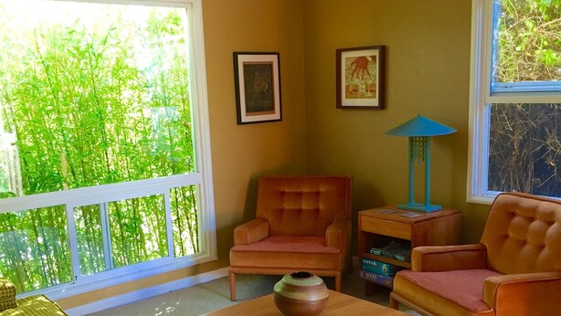 A living room with a sofa, two armchairs, a coffee table, and a lamp. There are framed pictures on the wall and a window with a view of greenery. - Redwood coast farm stay (Bayside)