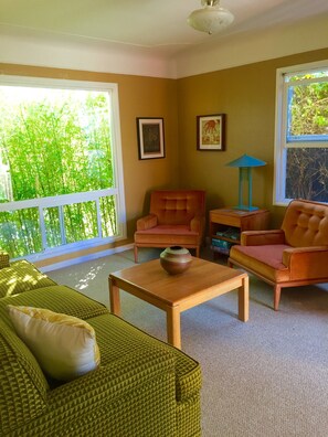 A living room with a sofa, two armchairs, a coffee table, and a lamp. There are framed pictures on the wall and a window with a view of greenery. - Redwood coast farm stay (Bayside)