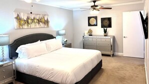 Quarto com cama, duas mesas de cabeceira, cômoda, duas ventoinhas no teto e obras de arte nas paredes.