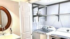 Uma área de lavanderia com máquina de lavar, secadora e prateleiras para pendurar roupas.