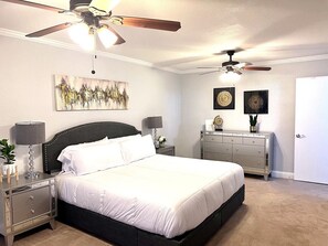 Un dormitorio con cama, mesitas de noche, cómoda y ventiladores de techo.