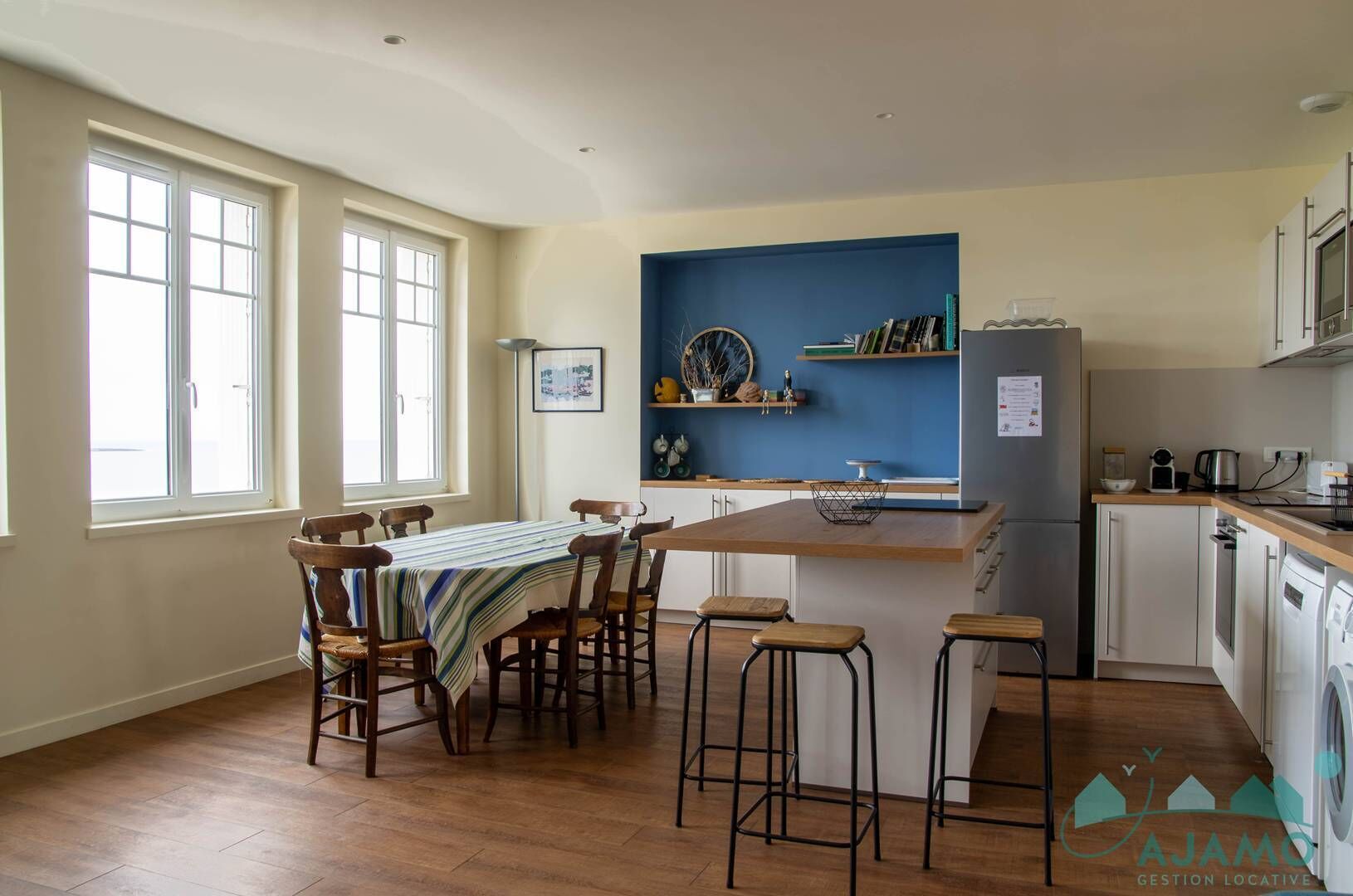 A modern kitchen with a wooden dining table, bar stools, and a blue accent wall.