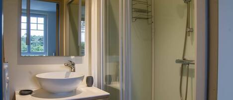 Un baño con un lavamanos grande de color blanco, un espejo y una zona de ducha con paredes de vidrio.