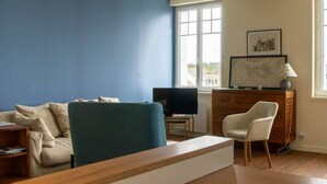 Una sala de estar con pared azul, piso de madera, un sofá, una silla, un televisor y un mueble de madera.
