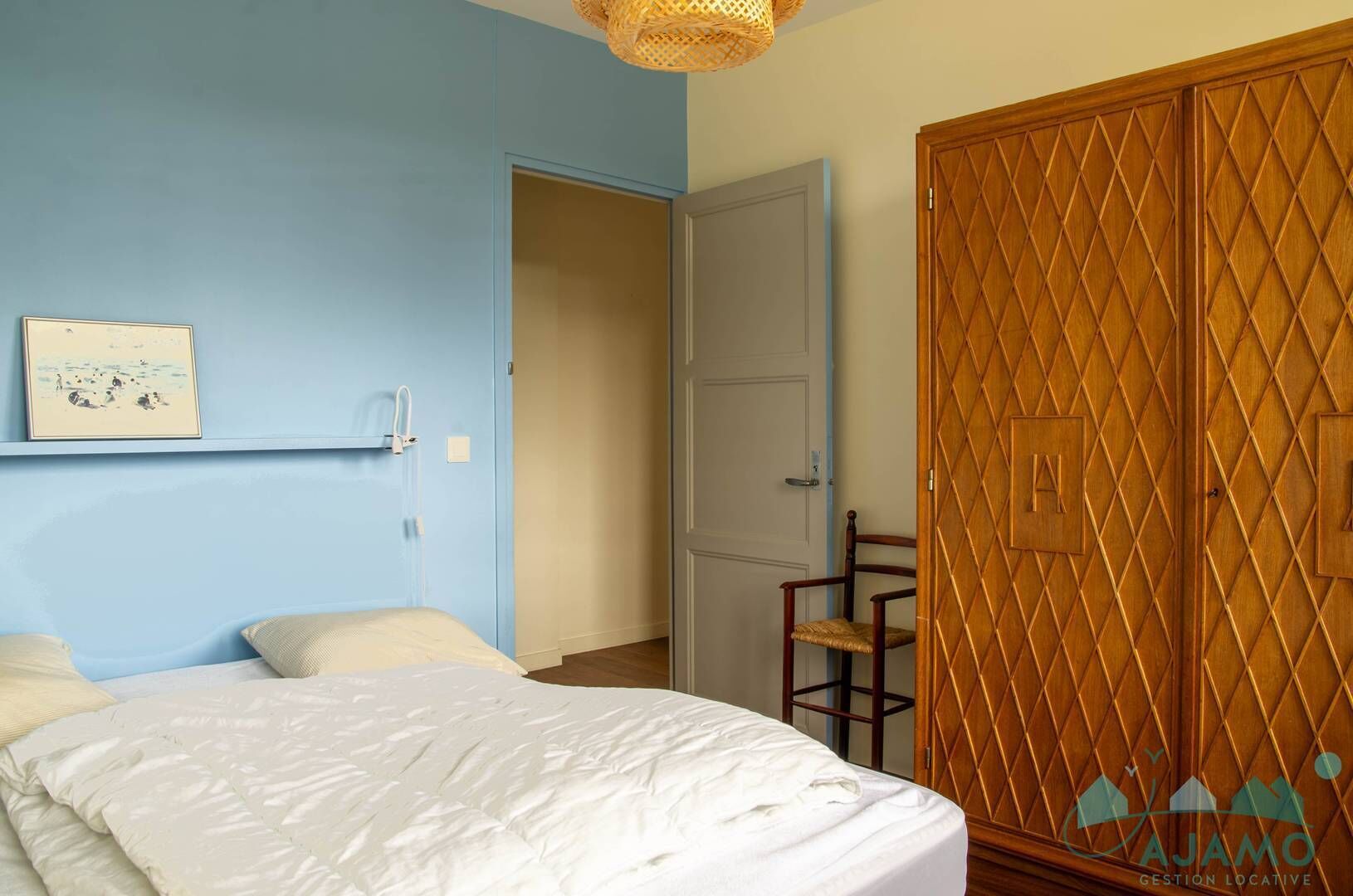 Un dormitorio con una cama, un armario de madera, una silla y una estantería en la pared con un cuadro.
