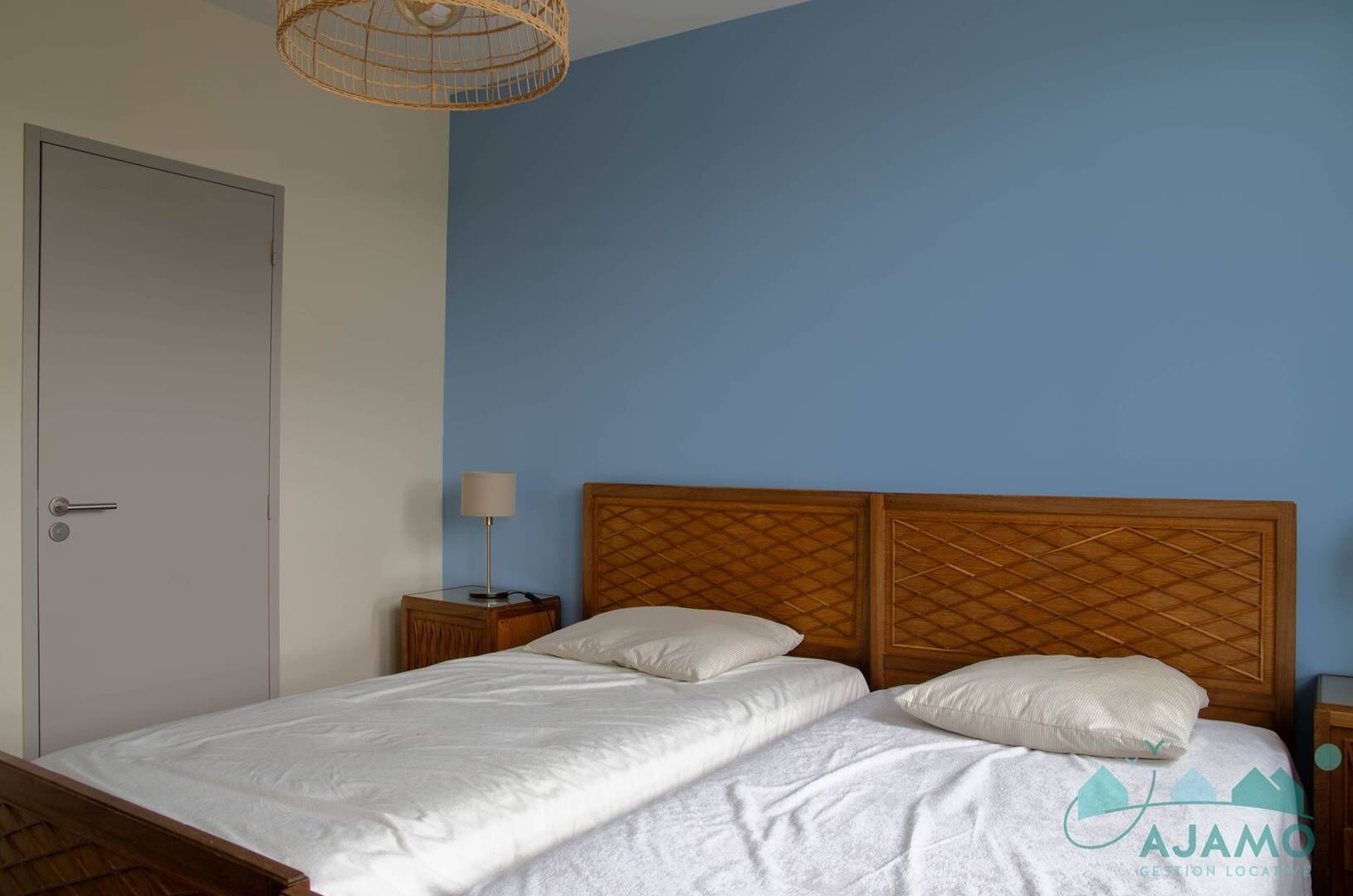 Quarto com cama, mesa de cabeceira, abajur e porta.