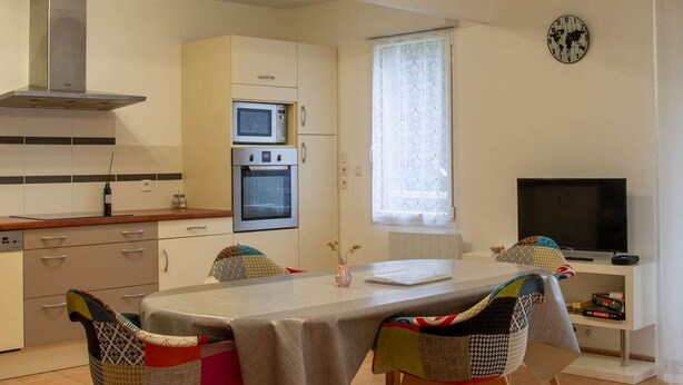 Eine kompakte Küche mit Mikrowelle, Backofen und einem großen Fenster. Ein Esstisch mit Stühlen und ein Fernseher stehen in der Ecke.