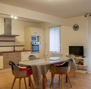 A compact kitchen with a microwave, oven, and a large window. There is a dining table with chairs and a television in the corner.