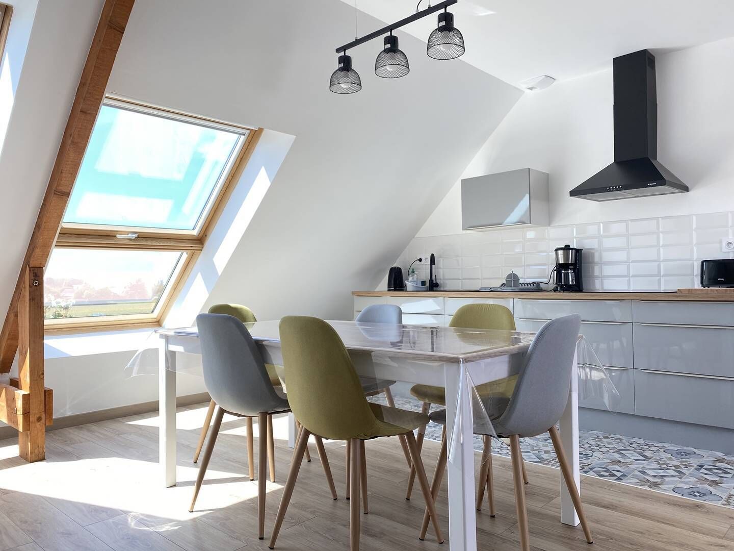 Een moderne keuken met een eethoek, voorzien van een dakraam, een zwarte afzuigkap en een betegelde achterwand.
