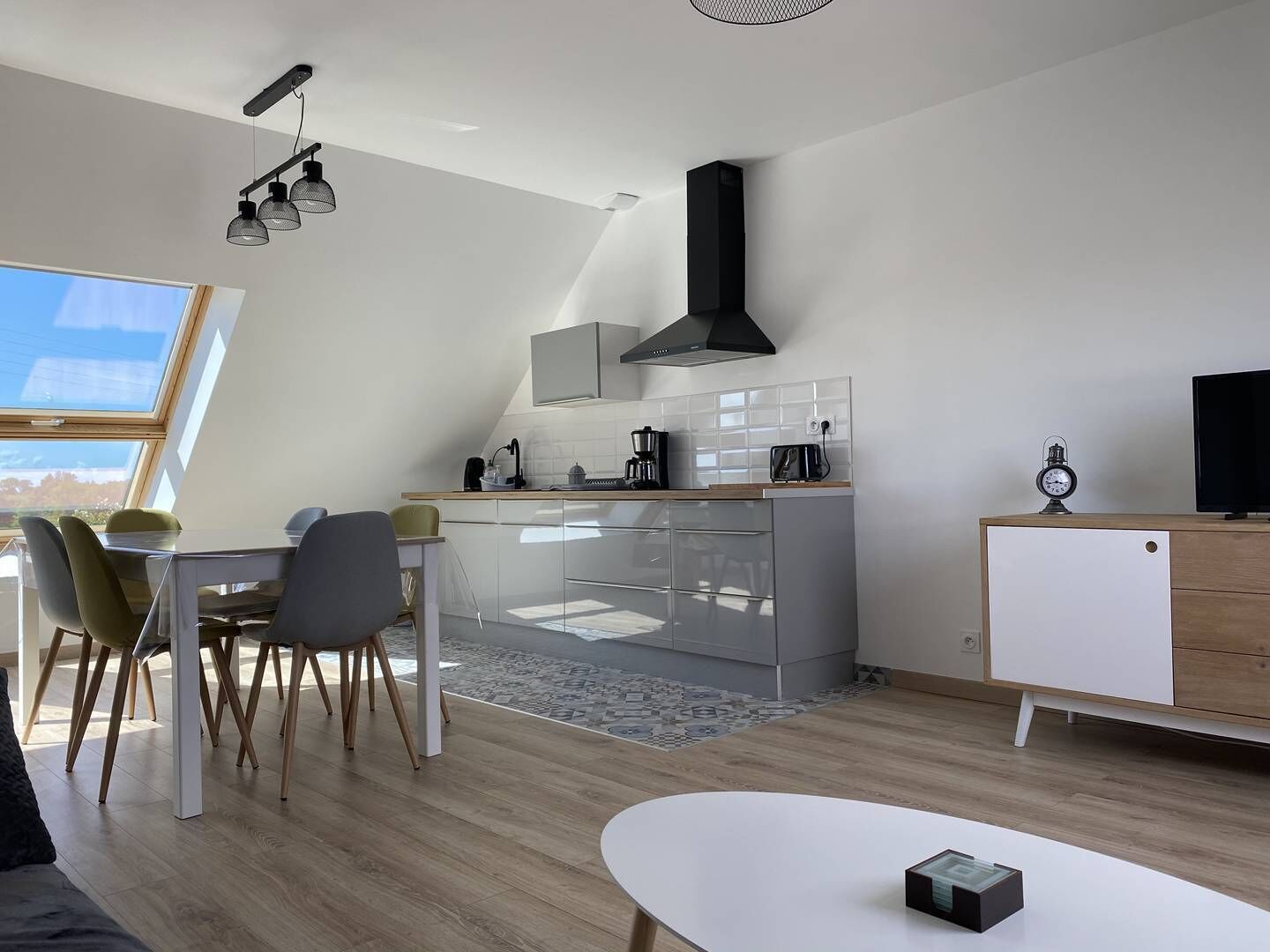 A modern kitchen with a dining area, a TV, and a clock on a cabinet.
