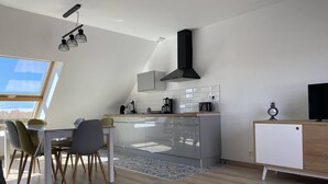A modern kitchen with a dining area, a TV, and a clock on a cabinet. - Family apartment with terrace in Fréhel | 6 guests | Ref 303 (FREHEL)