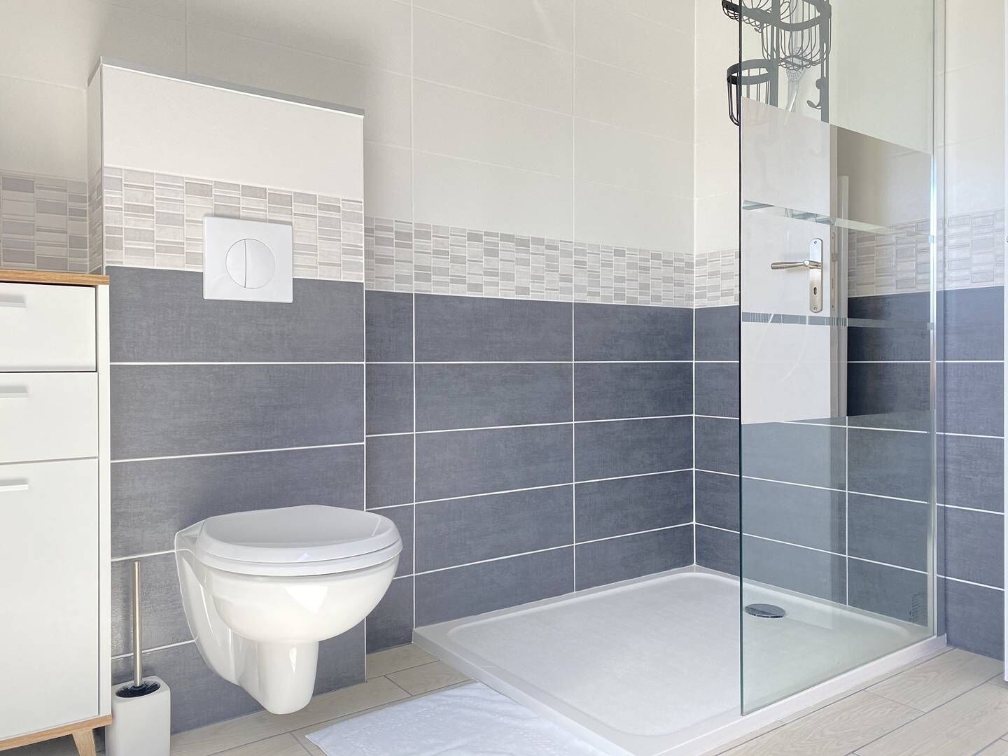 Une salle de bain moderne équipée de toilettes, d’une douche avec une porte en verre et d’un mur recouvert de carreaux.