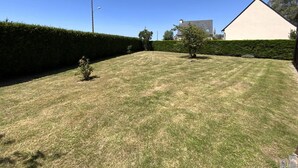 A well-maintained lawn with a hedge, a small tree, and a building in the background. - Family apartment with terrace in Fréhel | 6 guests | Ref 303 (FREHEL)