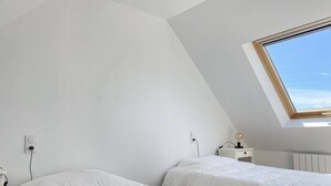 A bedroom with two beds, a skylight, and a bedside table with a lamp. - Family apartment with terrace in Fréhel | 6 guests | Ref 303 (FREHEL)