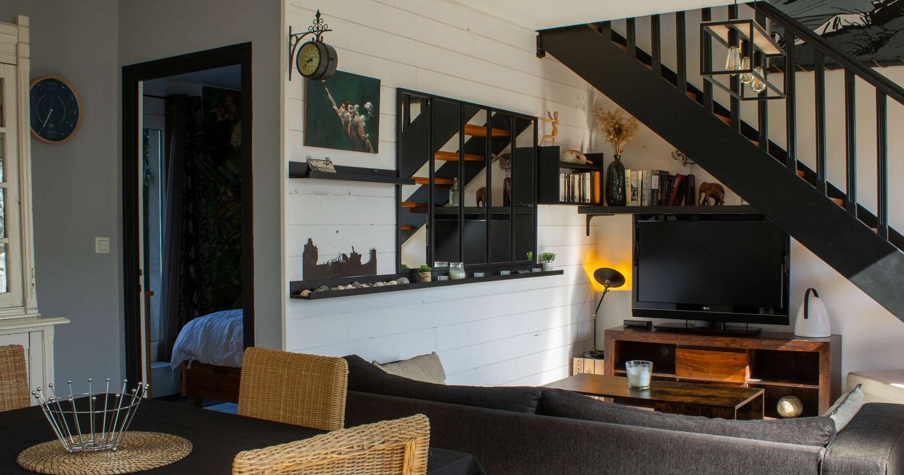 A modern living room with a staircase, a flat-screen TV, and a bookshelf.
