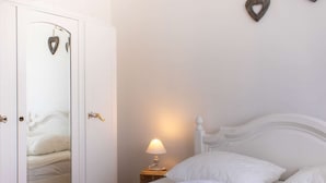 Un dormitorio con una cama blanca, una lámpara de noche y un armario con espejo.