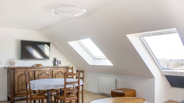 Une pièce avec un plafond en pente, une table à manger avec des chaises, un téléviseur et un radiateur.