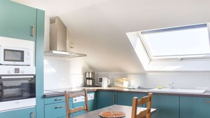 Une cuisine compacte dotée d’un puits de lumière, d’un four Bosch, d’une machine à café et de meubles de couleur turquoise.
