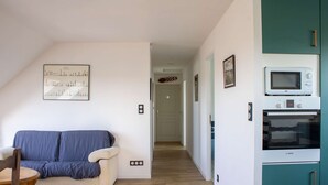 Un salon avec un canapé bleu, une chaise en bois, une cuisine équipée d’un four Bosch et un four à micro-ondes Bosch fixé au mur.