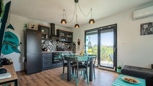 A modern kitchen with dark cabinetry, a dining area with teal chairs, and a balcony with a hanging chair.