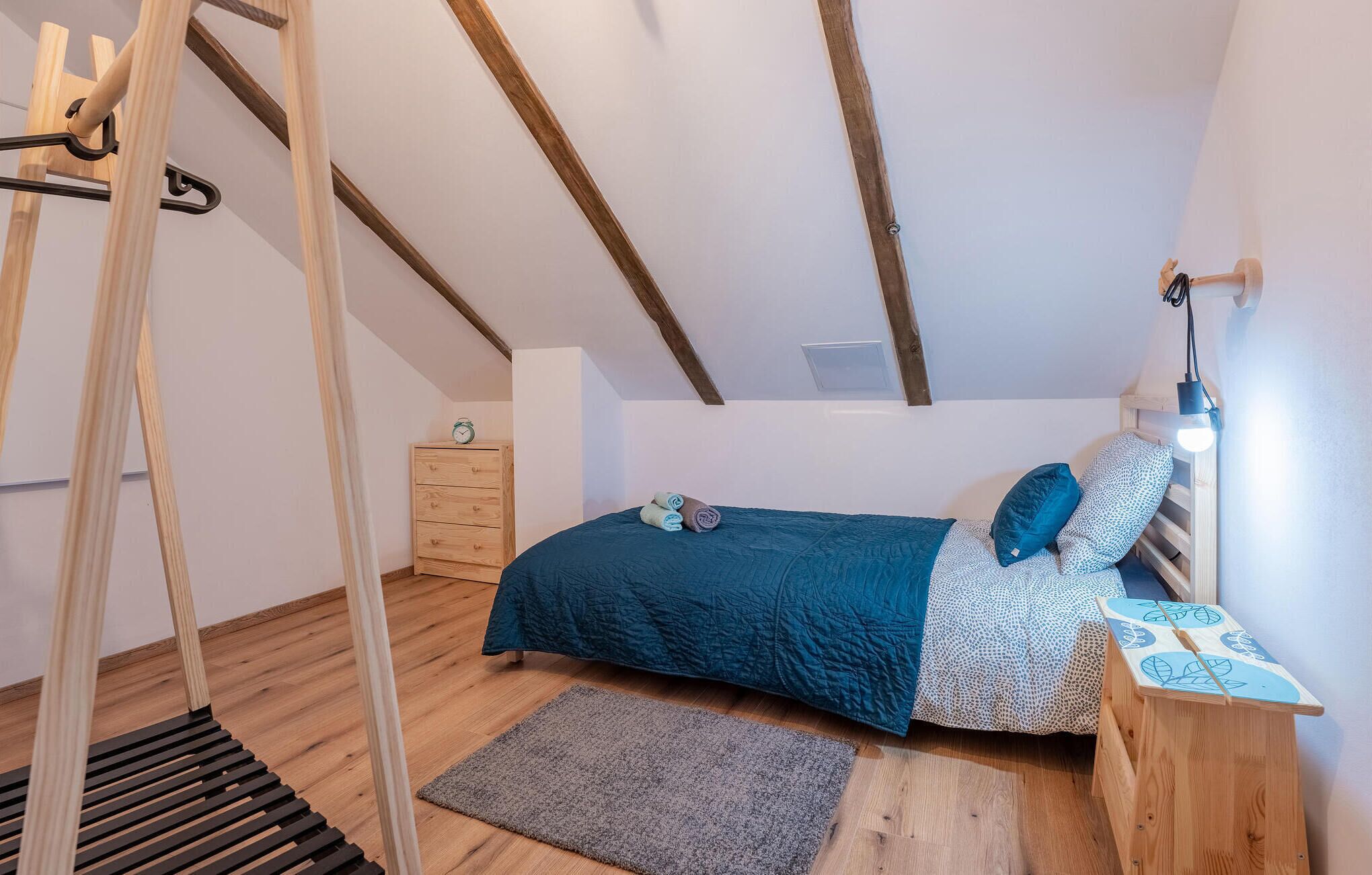 A bedroom with a bed, a wooden dresser, a nightstand, a lamp, a clock, and a wooden swing.