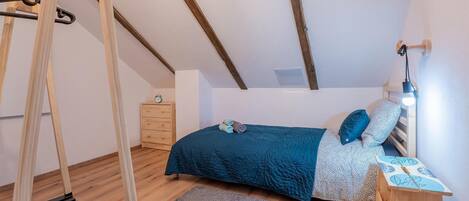 A bedroom with a bed, a wooden dresser, a nightstand, a lamp, a clock, and a wooden swing.
