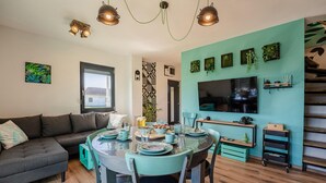 A modern living room with a grey sofa, teal dining table, and a TV mounted on a teal wall.