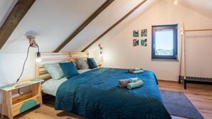 A cozy loft bedroom with a sloped ceiling, a wooden bed frame, a blue quilted bedspread, and a small wooden nightstand with a lamp.