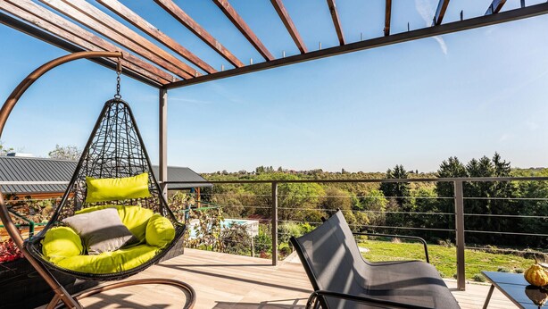 A balcony with a hanging chair, a lounge chair, and a view of a pool and greenery.