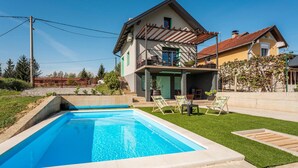 A two-story house with a swimming pool, a balcony, and a garden.