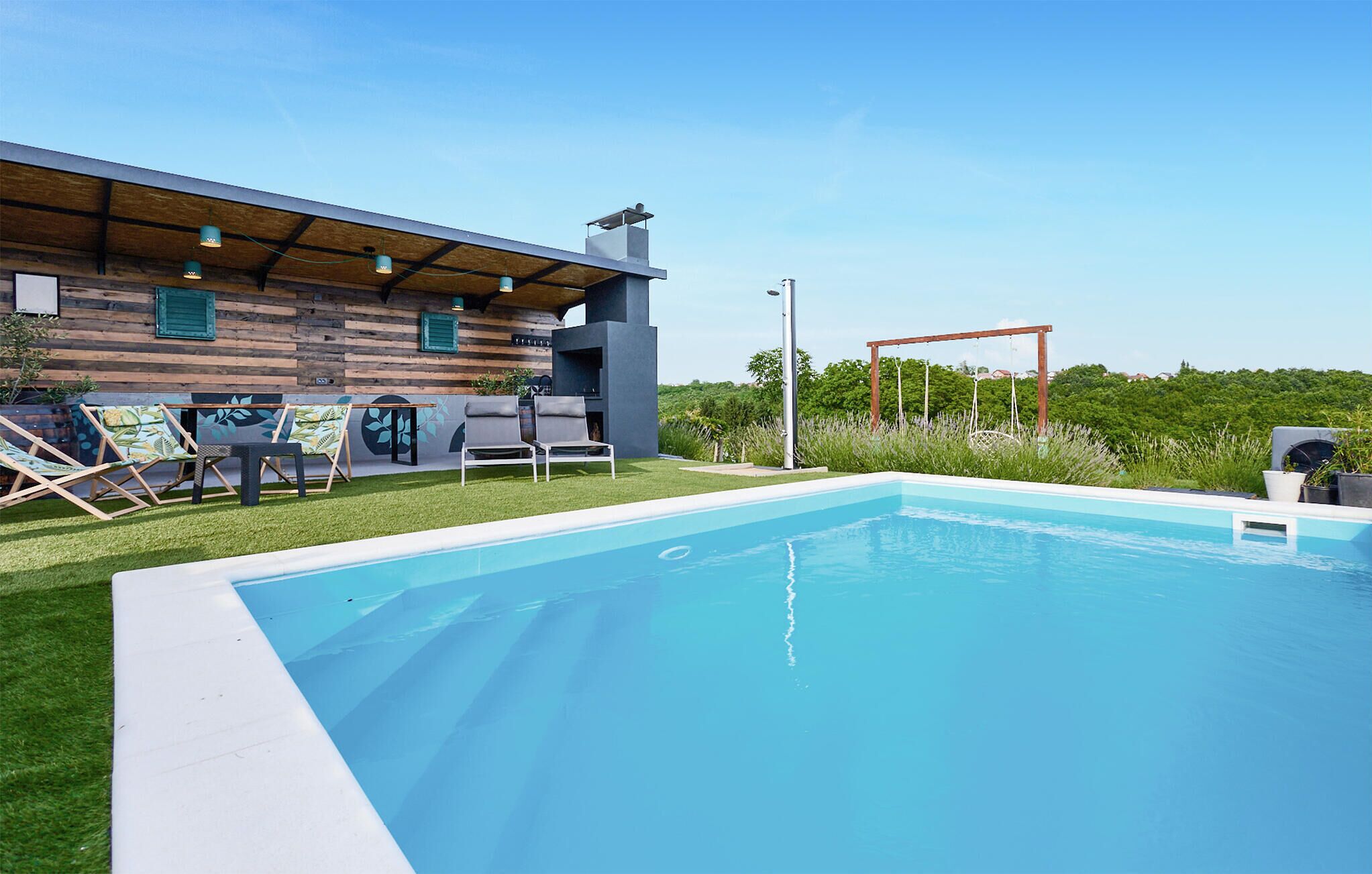 A modern outdoor pool area with a wooden deck, lounge chairs, and a barbecue grill.