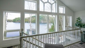 Habitación con amplios ventanales que dan a un lago, una escalera y vistas al exterior.