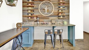 A kitchen with a central island, bar stools, a wine rack, and a decorative tree wall piece.
