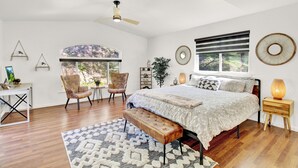 A bedroom with a bed, a desk, a chair, a bench, and a window.