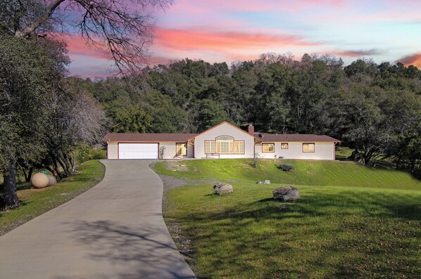 A single-story house with a garage, surrounded by a grassy lawn and trees.
