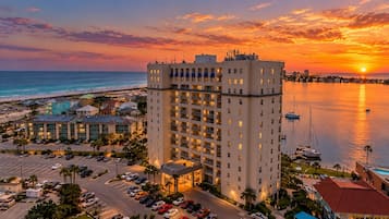 A high-rise hotel with multiple floors, a parking lot, and a view of the ocean at sunset.