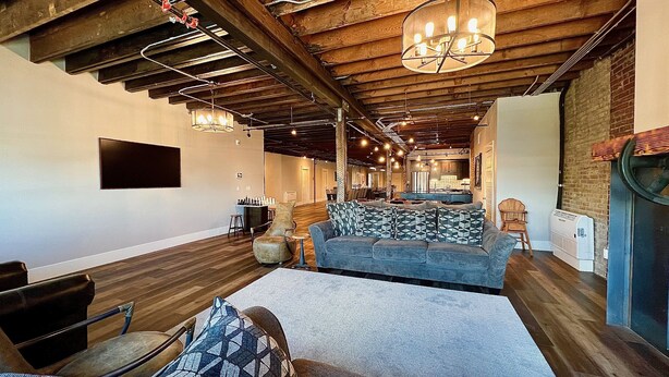 A spacious living area with a sofa, chairs, and a fireplace. There is a kitchen in the background with wooden cabinets and a dining area. - Modern Luxury Meets Historic Charm: Unwind in Style in Purpose Executive Suites (Pocatello)