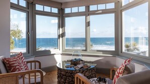 A room with a large bay window overlooking the ocean, a round glass table with a rustic stone base, and two wooden chairs. - The Croft is a beautiful four bedroom detached retreat near Coverack. (The Lizard)