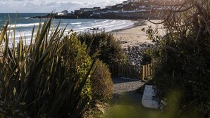 A coastal view with a beach, rocky shoreline, and a path leading to a wooden fence. - The Croft is a beautiful four bedroom detached retreat near Coverack. (The Lizard)