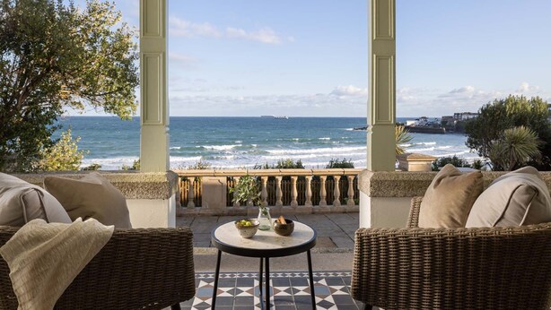 A balcony with wicker furniture and a tiled floor, overlooking the sea and a coastal town. - The Croft is a beautiful four bedroom detached retreat near Coverack. (The Lizard)
