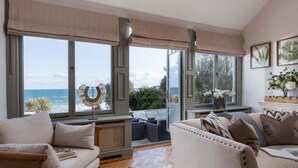 A spacious living room with a large window overlooking the sea, a cozy sofa, and a fireplace with decorative items. - The Croft is a beautiful four bedroom detached retreat near Coverack. (The Lizard)