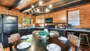 A modern kitchen with wooden cabinets, a black refrigerator, a dining table set with white plates, and a potted plant. - Cabin With Amazing Mountain Views! Sleeps 8! 8 Mins From The Strip! (Sevierville)