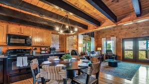 A spacious kitchen with wooden cabinets, a microwave, and a dining area with a round table and chairs. - Cabin With Amazing Mountain Views! Sleeps 8! 8 Mins From The Strip! (Sevierville)